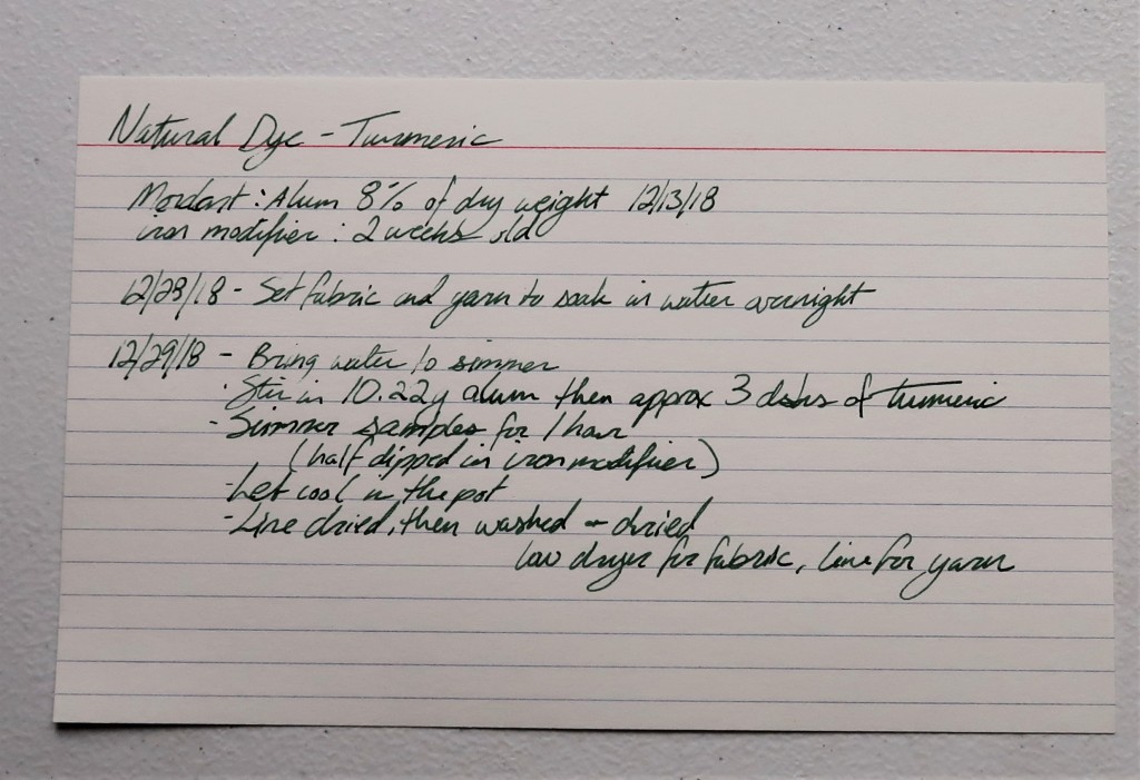 An index card on a white table. The information for the Turmeric dye transcribed to this website is written in black ink.